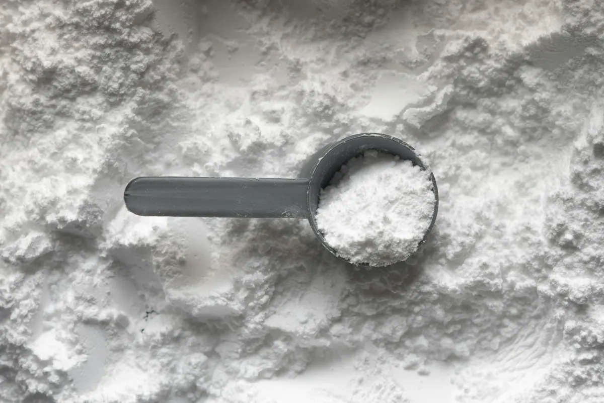 Creatina monohidrato junto a un vaso de agua y material de entrenamiento